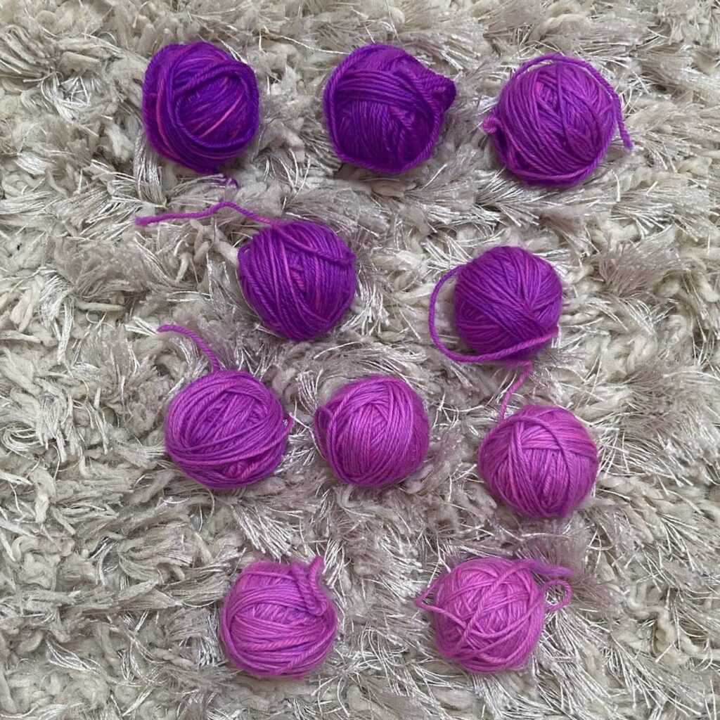 10 motków wełny w rożnych odcieniach fioletu.